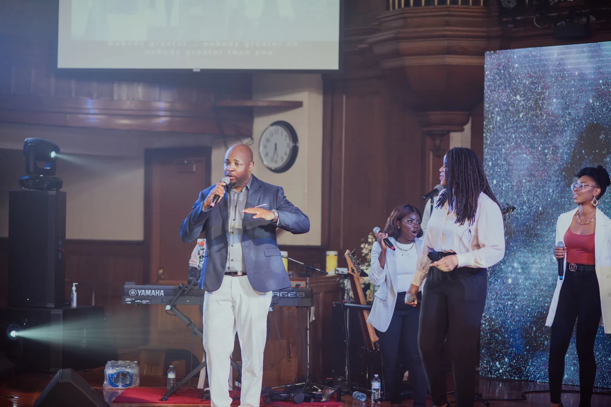Maxwell AU leading worship with backing vocalists in a wood-panelled hall.